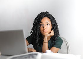 Young woman with glasses working attentively on a laptop at a bright desk.